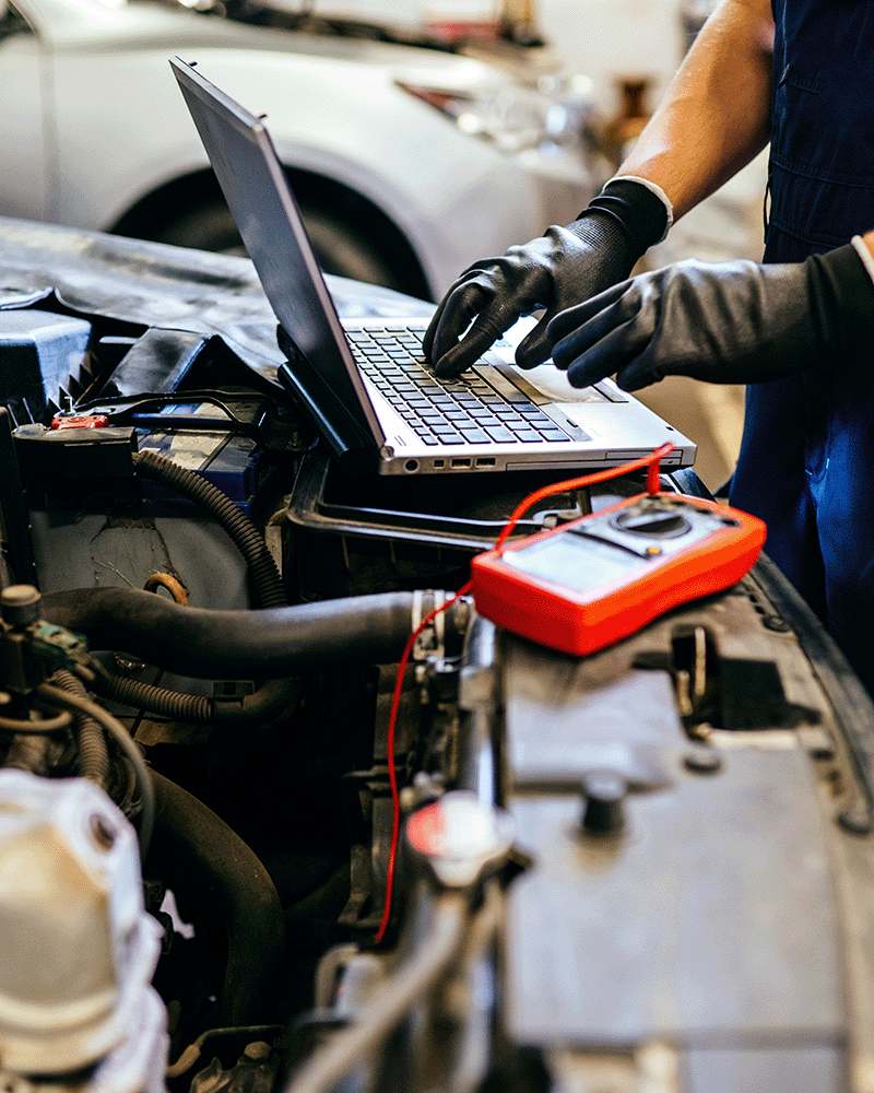 Mechanic reviewing diagnostic software on a laptop connected to a car in the workshop
