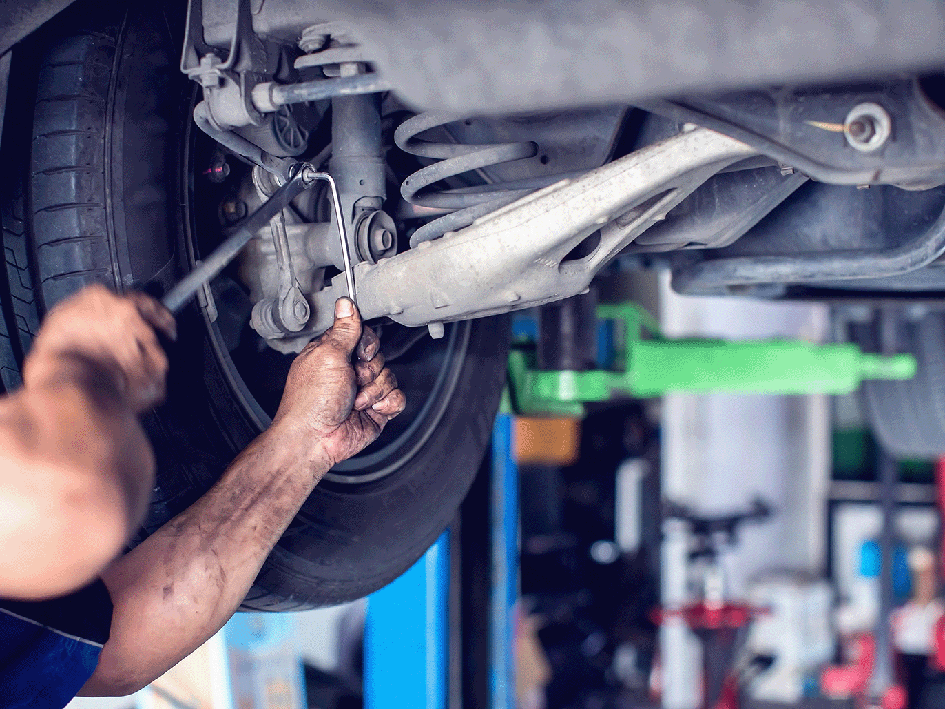 Mechanic checking a car's suspension setup on a ramp in the workshop